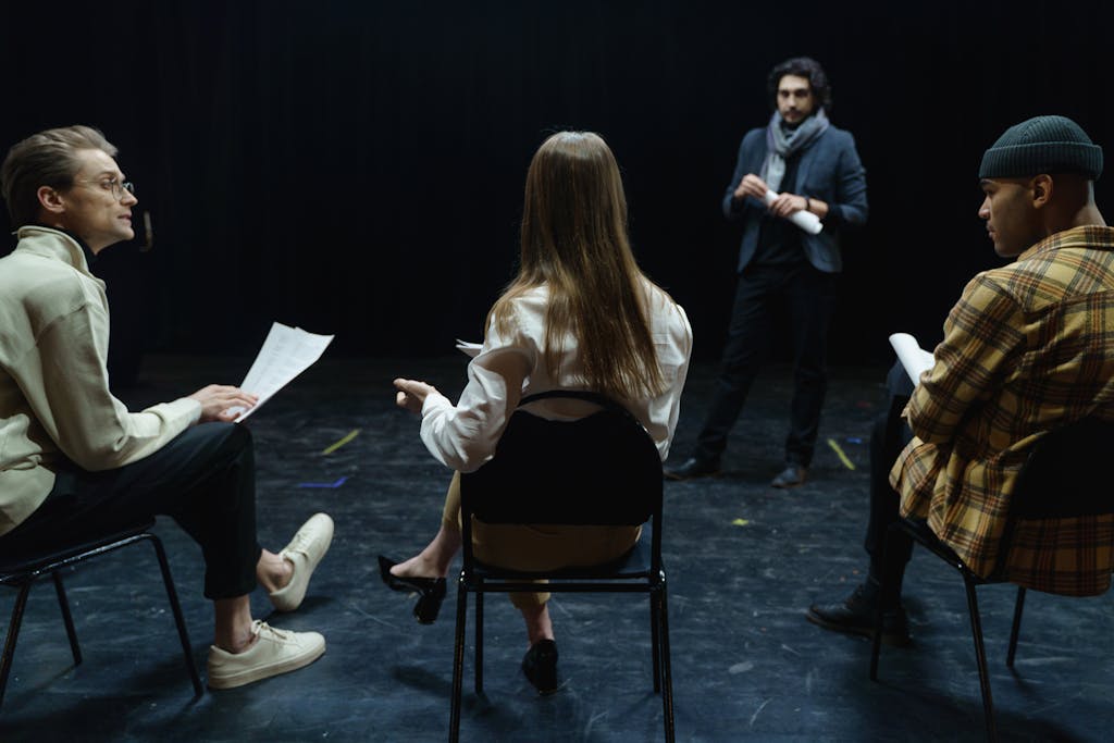 Group of actors in rehearsal with director, practicing for a theater performance.