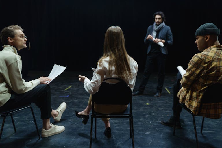 Group of actors in rehearsal with director, practicing for a theater performance.