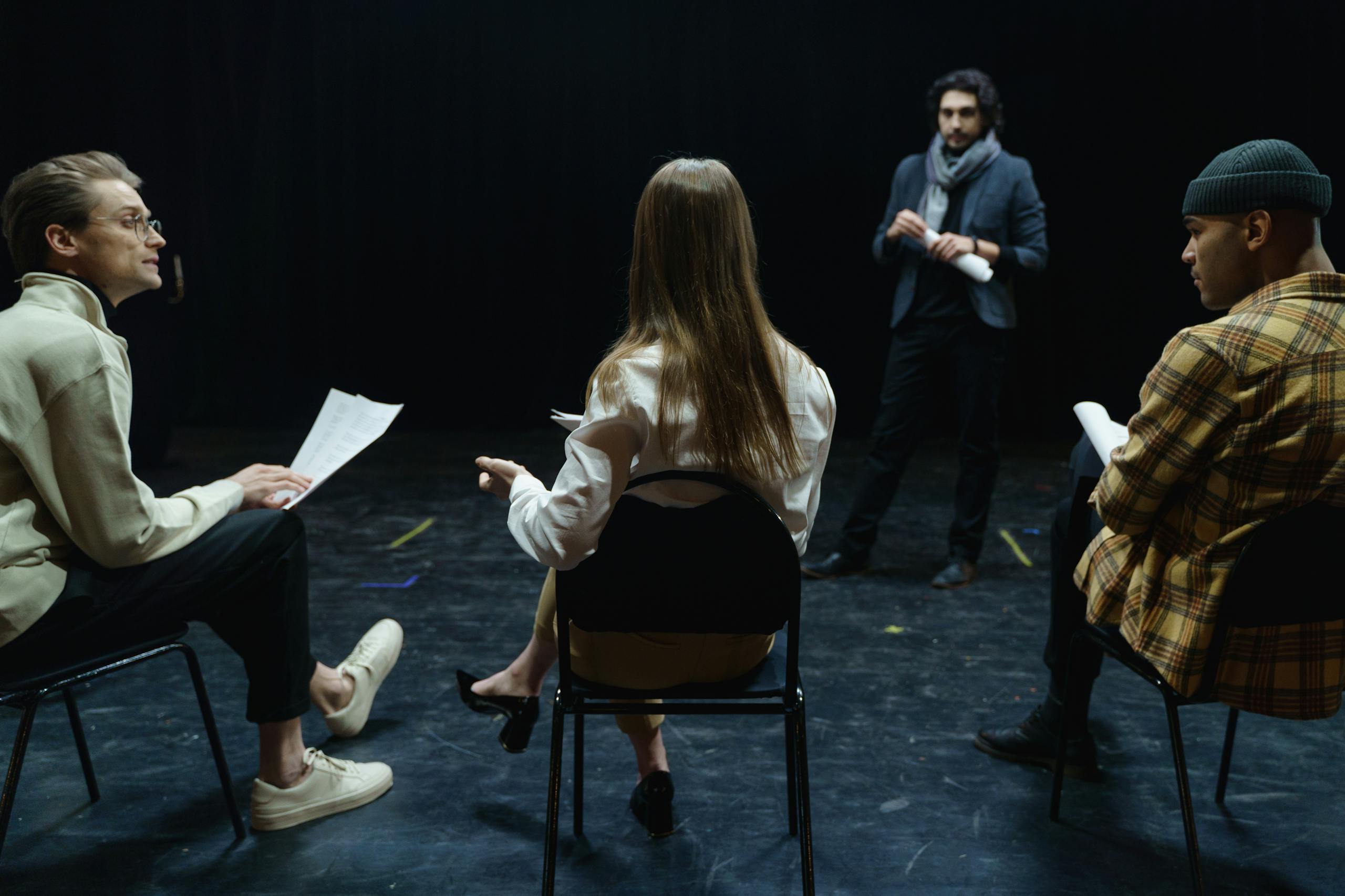 Group of actors in rehearsal with director, practicing for a theater performance.