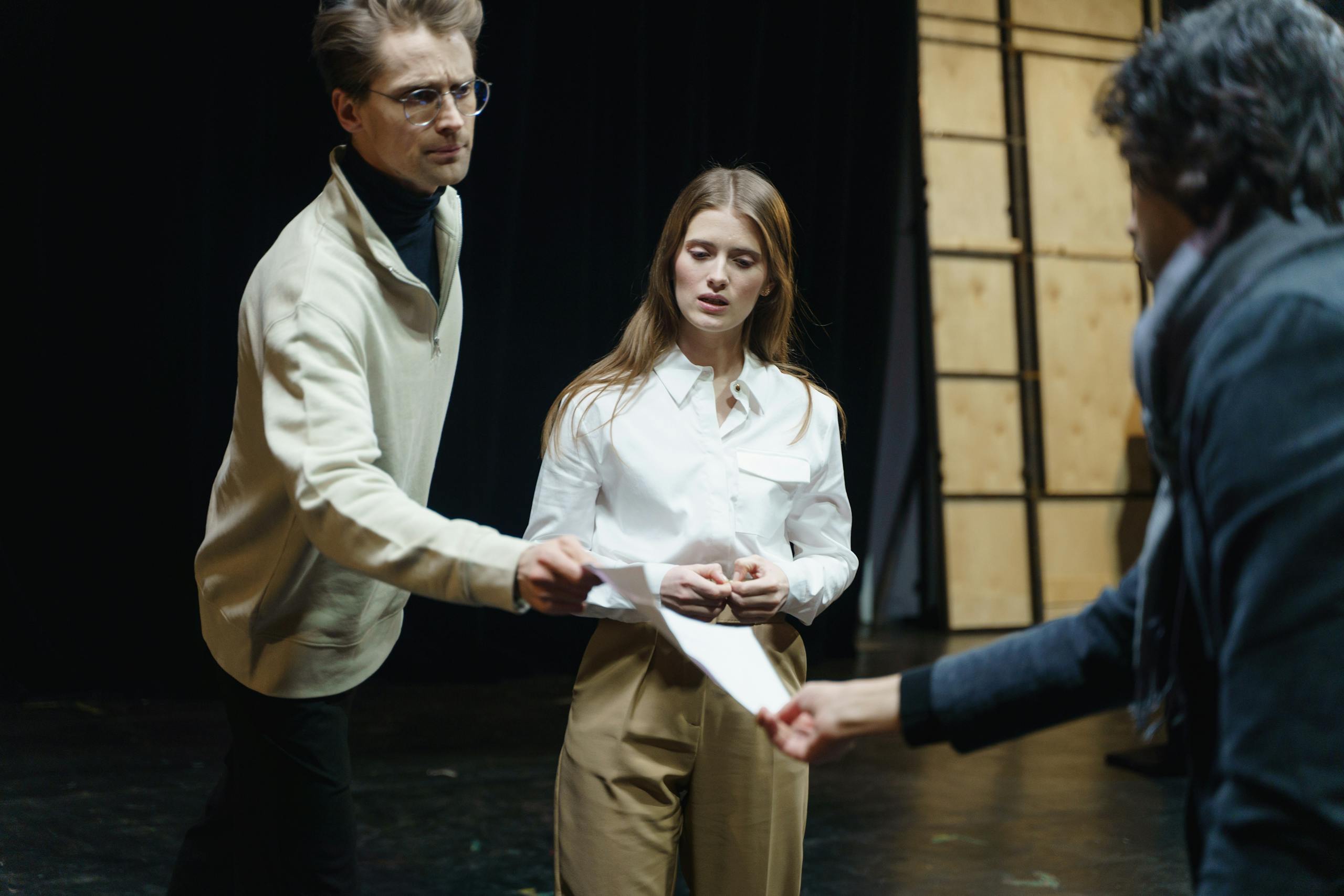 Actors engage in a rehearsal, exchanging scripts on stage, embodying theatrical drama and emotion.