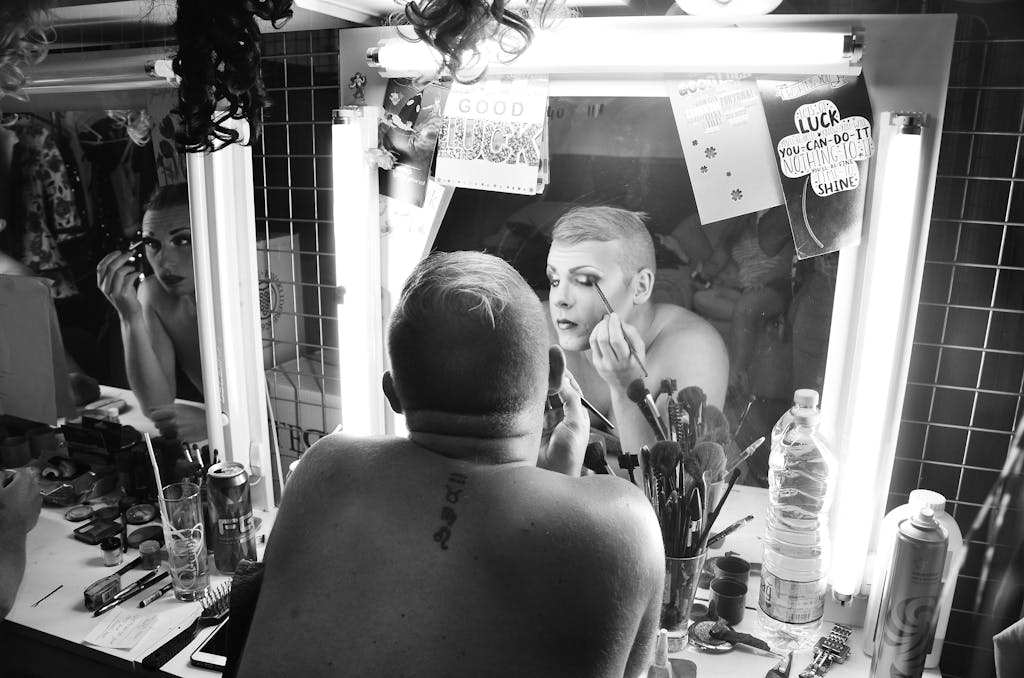 Drag queen applying makeup in dressing room, showcasing artistry and transformation.